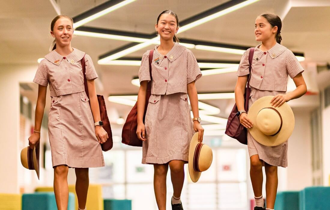 澳洲 莫頓灣女子學校 MBC 學生走廊合影：三名身穿典雅粉色制服、戴著特色草帽的女學生自信開心地走在校園中。MBC 專注於 頂級女校全人教育，培養女孩大方優雅與自主學習氣質。